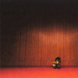 Person sitting on a red carpet in front of a dark wall with a subtle pattern