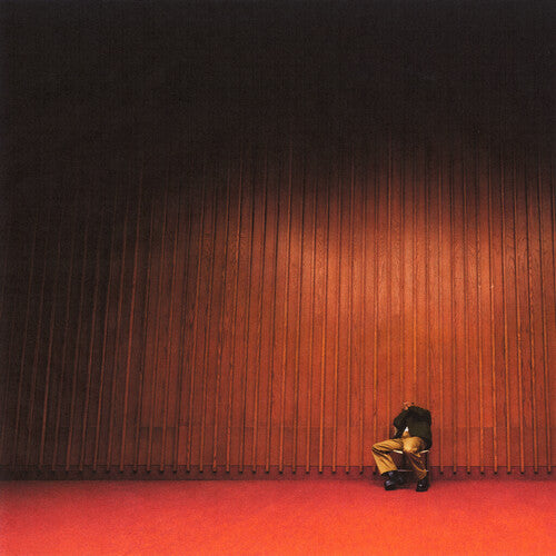 Person sitting on a red carpet in front of a dark wall with a subtle pattern