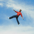 Man in a red sweater and blue jeans floating against a blue sky with white clouds