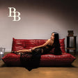Woman sitting on a red leather sofa in a dimly lit room with a minimalistic background.