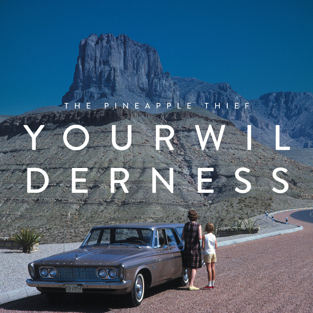 Album cover for 'Your Wil Derness' by The Pineapple Thief, featuring a vintage gray car parked on a desert road with two people standing beside it in front of a large rock formation under a clear blue sky.
