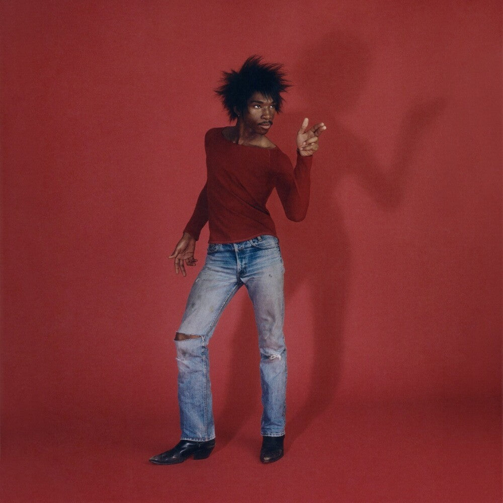 A person posing in a dark red long-sleeve top and light blue ripped jeans against a solid red studio backdrop.
