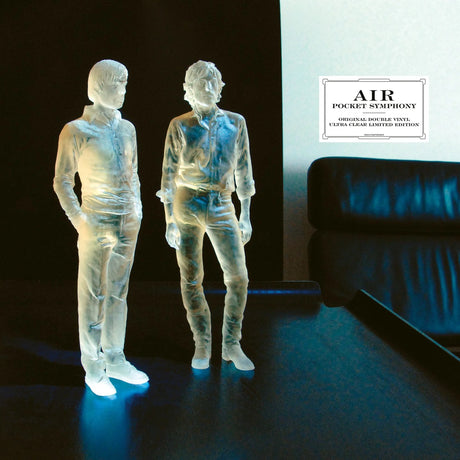 Clear plastic figures of two people on a dark surface with 'AIR' album cover in the background.