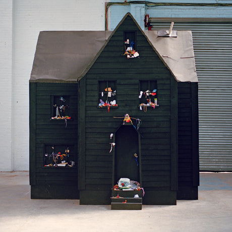 Dark wooden playhouse with small figures and objects on shelves against a plain background