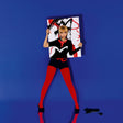 Person in black and red outfit holding a colorful abstract painting against a blue background