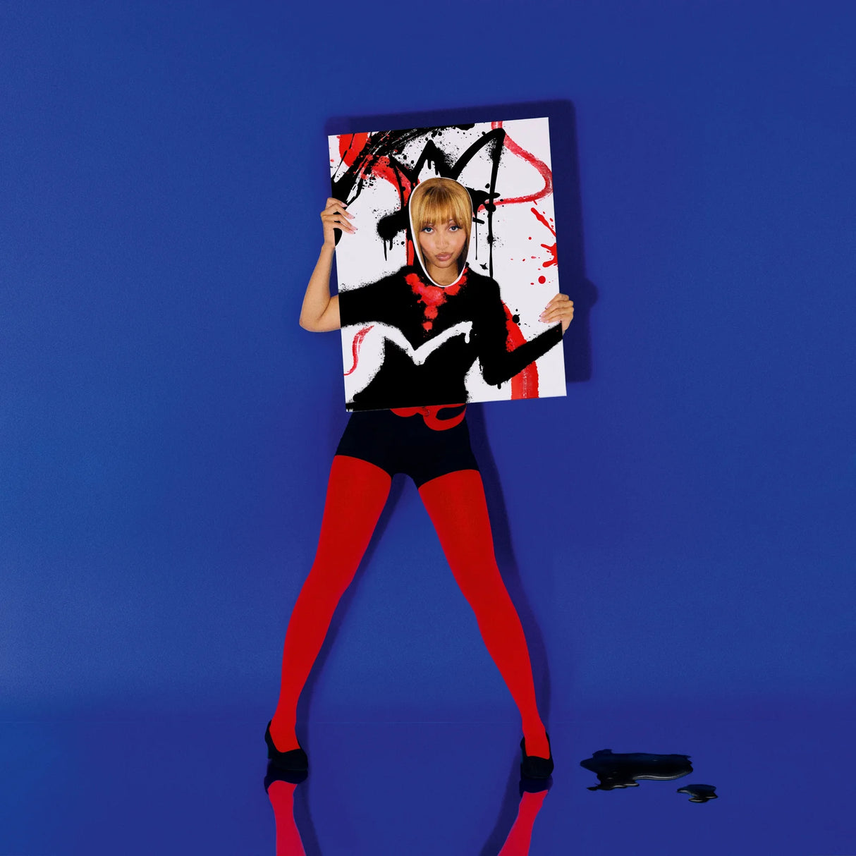 Person in black and red outfit holding a colorful abstract painting against a blue background