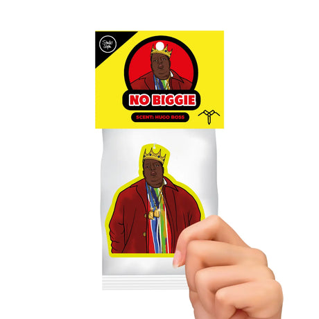 A hand holding a small printed card or sticker featuring an illustrated figure in a red jacket and gold crown, with a bright yellow header that reads 'NO BIGGIE' and 'SCENE: HUGO ROSS'.