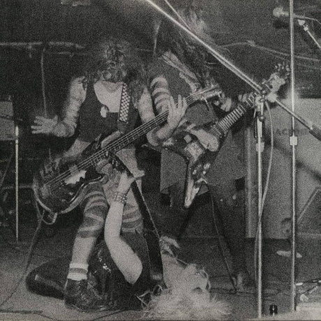 Two musicians playing electric guitars on stage with a microphone stand in the foreground.
