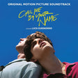 This image features the limited edition pink vinyl soundtrack for the film "Call Me By Your Name." The album cover displays a captivating photo of two young men, elegantly dressed, sharing a intimate and joyful moment against a bright blue backdrop.