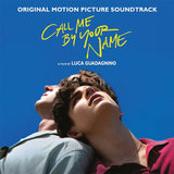 This image features the limited edition pink vinyl soundtrack for the film "Call Me By Your Name." The album cover displays a captivating photo of two young men, elegantly dressed, sharing a intimate and joyful moment against a bright blue backdrop.