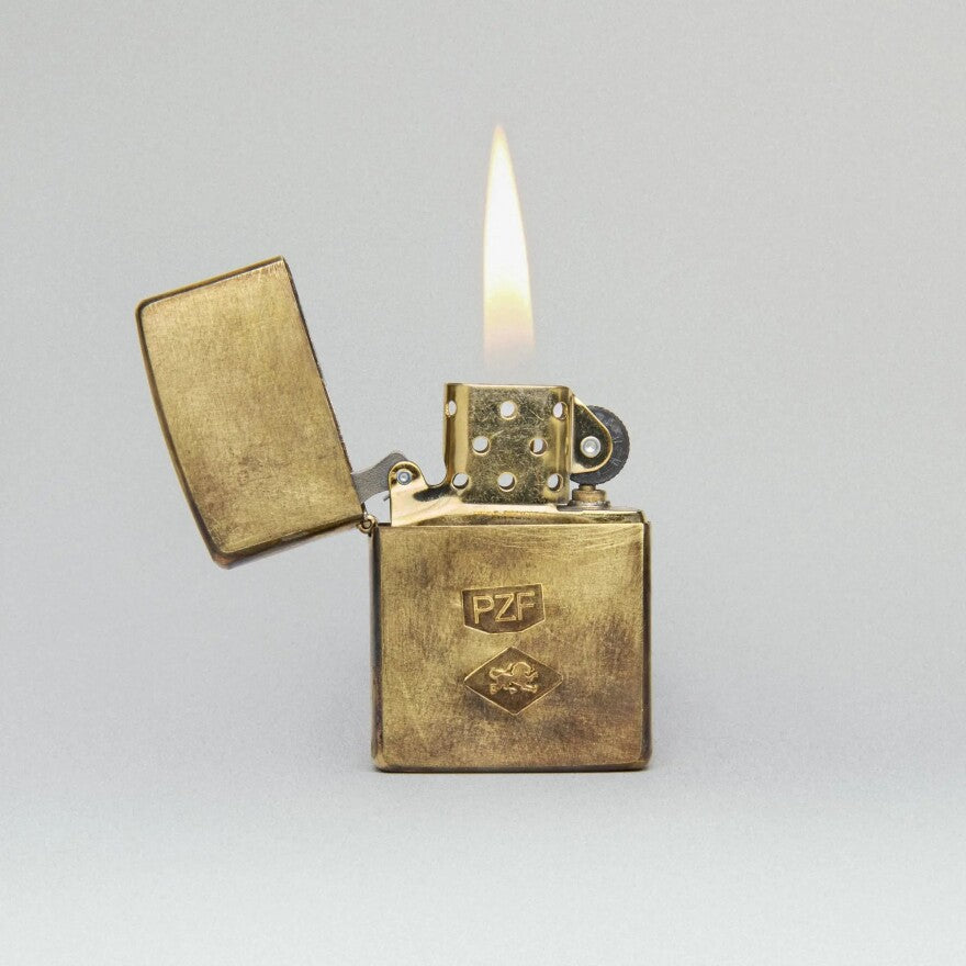 Brass zippo lighter with 'PZF' logo on a gray background