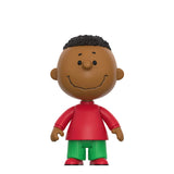 A stylized vinyl figure of a cartoon boy with brown skin, black curly hair, a red shirt, and green pants, centered on a plain white background.