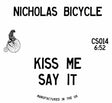 A square white product label or packaging card with bold black text reading 'NICHOLAS BICYCLE' at the top and 'KISS ME SAY IT' in the center. A small black line drawing of a person riding a penny-farthing bicycle appears on the left.