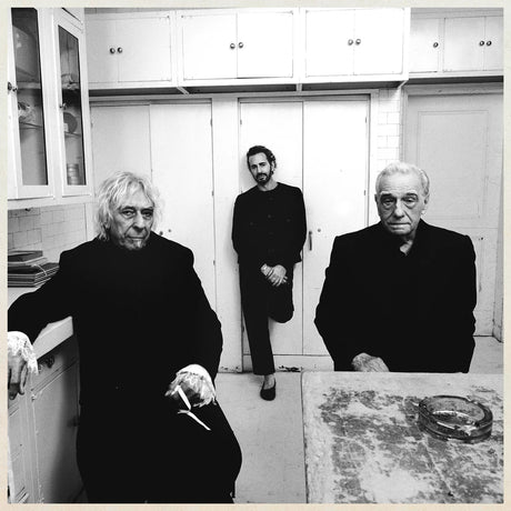 Three people in a kitchen setting, with white cabinets and a tiled wall.