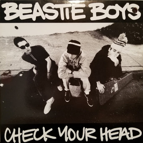 Album cover of 'Check Your Head' by Beastie Boys featuring three members sitting outdoors.