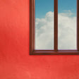 A window with a view of a cloudy sky, with the rest of the image showing a bright red wall.