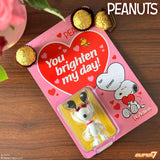 Peanuts-themed product packaging with Snoopy and a heart-shaped message on a wooden surface.