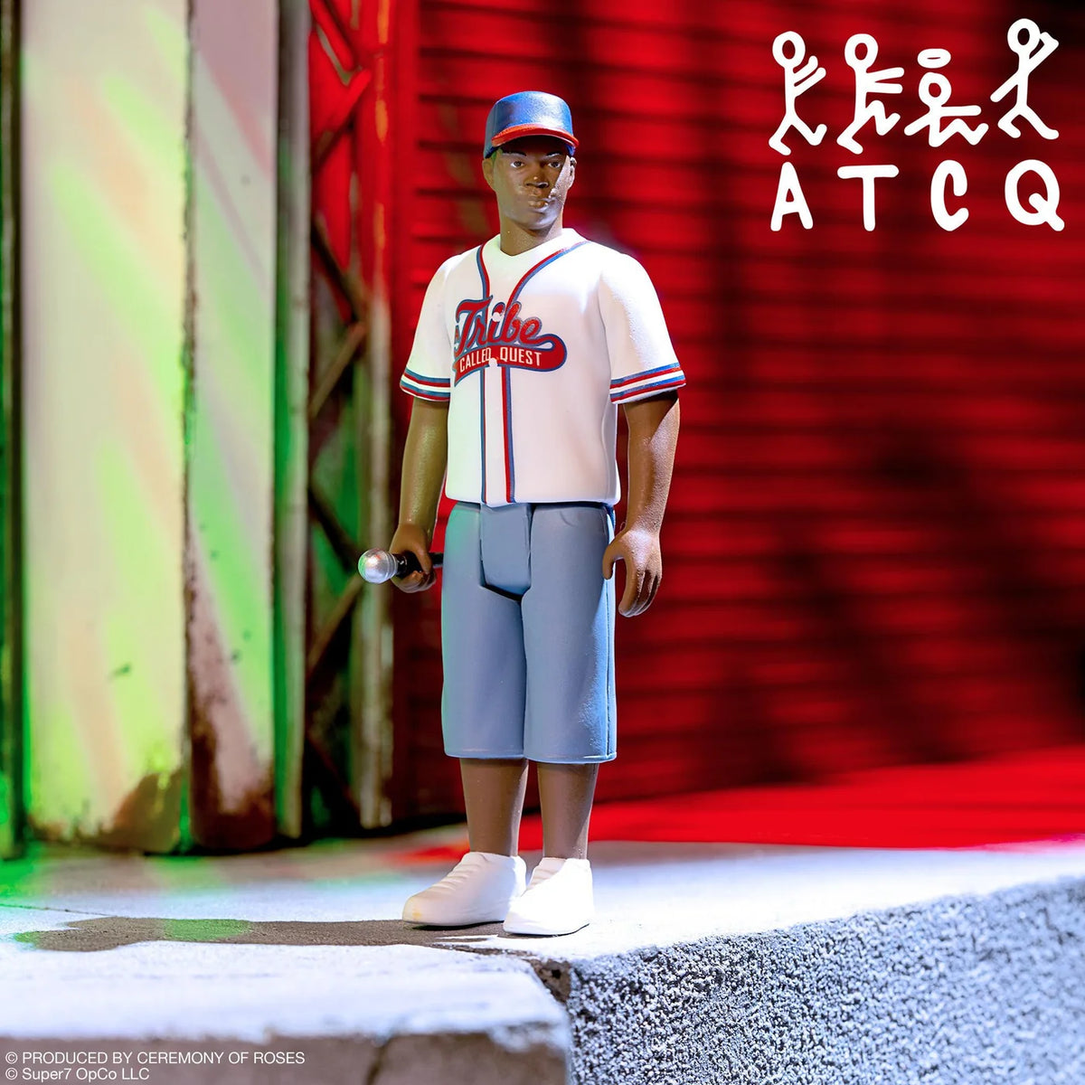 A detailed collectible action figure of a man wearing a baseball uniform and cap, standing on a concrete ledge with a microphone in hand, set against a red roller shutter background with stylized white text in the upper right.