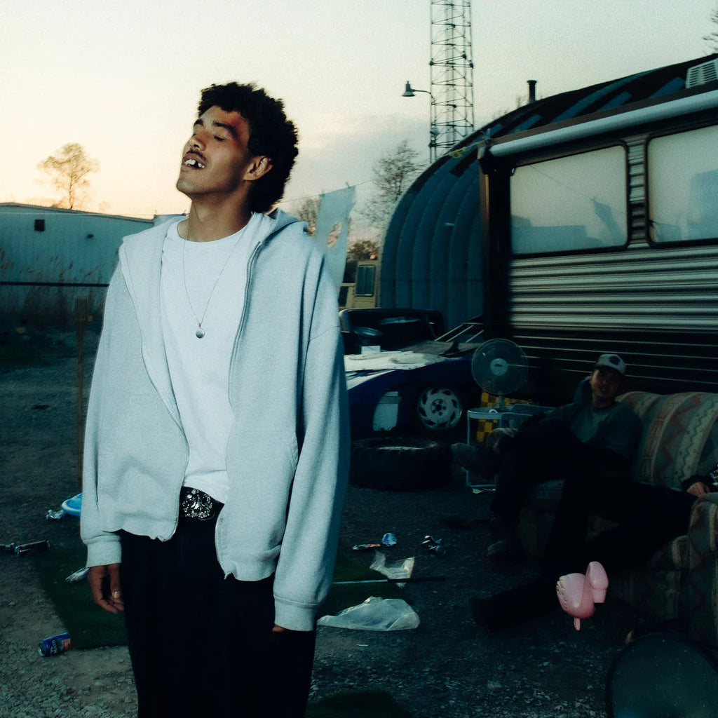 Man standing outdoors with a trailer and another person in the background