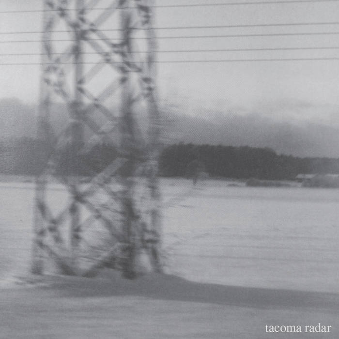 Black and white photograph of a large electricity pylon standing in a snowy landscape, with a line of trees in the background and the text 'tacoma radar' in the bottom right corner.