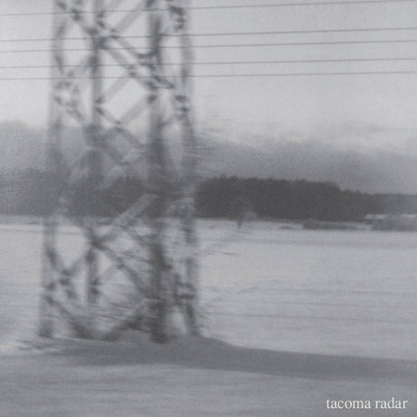Black and white photograph of a large electricity pylon standing in a snowy landscape, with a line of trees in the background and the text 'tacoma radar' in the bottom right corner.