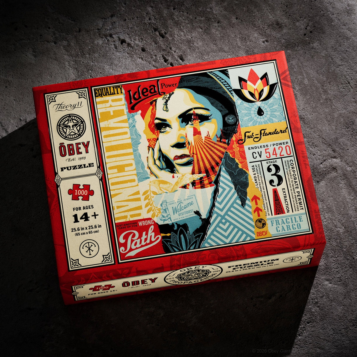 A boxed jigsaw puzzle package photographed on a dark textured surface. The box is red and cream with illustrated collage-style artwork featuring a woman's face, fan motifs, and text including 'Obey', 'Quality', '1000 pieces', and 'For ages 14+'.