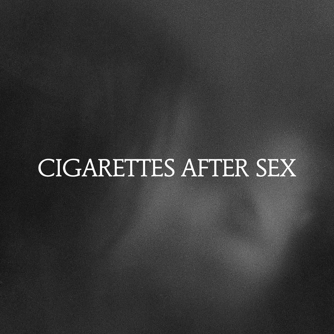 This image features the album cover for "Cigarettes After Sex - X's LP," which is described as an indie exclusive crystal clear vinyl release. The cover art is strikingly minimalistic and blurred, with the album title prominently displayed in a white serif font that stands out against the dark, indistinct background.