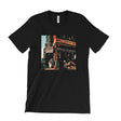 A black short-sleeve crewneck t-shirt featuring a square graphic print of a vintage street scene with a storefront and people, displayed flat against a solid white background.