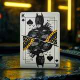 Playing card with a superhero design on a dark surface with blurred lights in the background