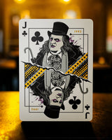 Playing card with a Jack of Clubs design featuring a character in a top hat and coat, with a blurred background.