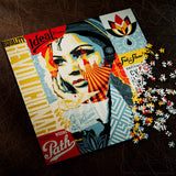 A completed jigsaw puzzle featuring a stylized pop-art portrait with bold red, yellow, blue, and cream sections, shown on a dark textured surface with loose puzzle pieces spilled to the right. Visible text includes 'Equality', 'Ideal Power', 'Wrong Path', and 'Subtlety'.