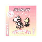Two enamel pins of cartoon characters on a 'Peanuts' Beach Club packaging with a pink and yellow gradient.