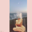 Person sitting on a fence with ocean waves crashing around, framed by a pink border.