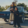Man holding a child and standing next to another child in front of a blue car on a road.