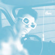 A person sitting inside a car, wearing oversized square white sunglasses, with the entire photo tinted in a strong light blue color.
