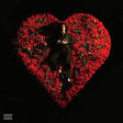 Person in a suit sitting on a heart-shaped arrangement of red roses against a black background
