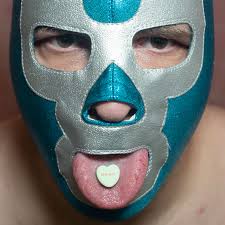 Person wearing a blue and silver mask with a heart-shaped candy on their tongue.