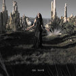 A woman in a long black dress stands in a dramatic outdoor landscape with tall rock spires and dry grass. The photo is mostly grayscale, with the title 'the dark' at the bottom.