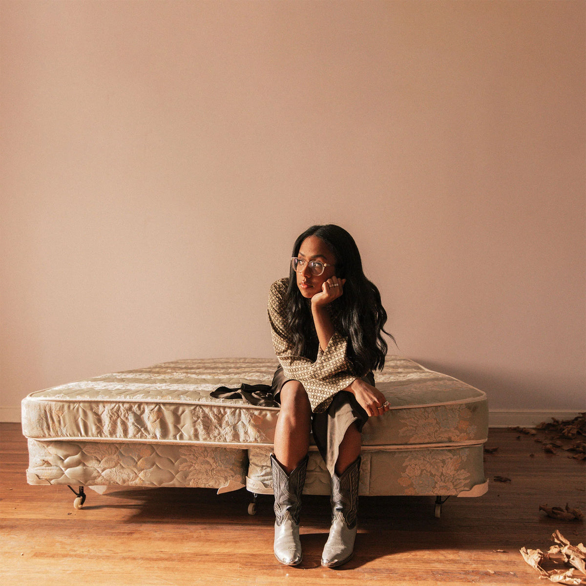 Woman sitting on a mattress in a minimalistic room with a beige wall.