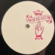 A close-up of a vinyl record label featuring a pink graphic of a hand holding a banner that reads 'MOB MUSEUM' under a crown, on a black vinyl disc.