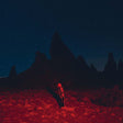 A person standing in a red-lit landscape with silhouetted rock formations in the background under a starry sky.
