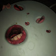 This image features the clear vinyl LP of Death Grips' album "Year of the Snitch." The album cover art is striking and controversial, depicting a close-up of a mouth with bloodstained teeth, surrounded by what appears to be a simulation of blood or liquid splatters across a grey background.