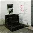 The image displays a vinyl record titled "IDLES - Brutalism LP," prominently featuring a photo of a woman on the cover. The cover is minimalistic, with the band's name and the album title in bold red and white text.