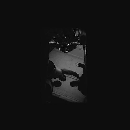 A black and white image of three people standing in the dark, with their backs to the camera, listening to something intently.