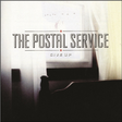 Album cover for The Postal Service's 'Give Up' featuring a dark and moody image with a piano and curtains.
